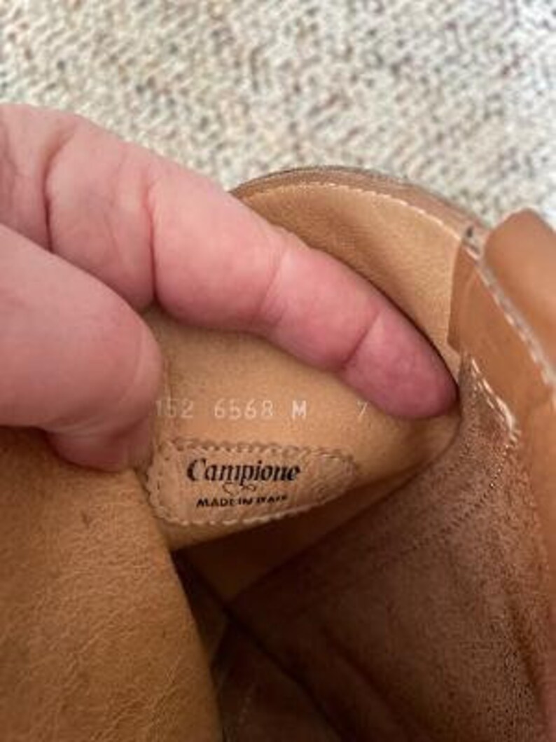 Puede incluir: Primer plano del interior de una bota de cuero marr&oacute;n con el texto "Campione Made in Italy" y los n&uacute;meros "152 6568 M 7" visibles.