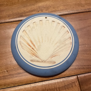 May include: A blue and white ceramic ornament with a raised seashell design. The ornament has a hole at the top for hanging.