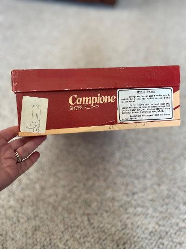 Puede incluir: Una caja de zapatos roja con las palabras "Campione Shoes" impresas en la parte delantera. La caja tiene una etiqueta blanca con informaci&oacute;n sobre los zapatos.