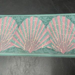 May include: A teal and pink seashell wallpaper border with a repeating pattern of three seashells. The seashells have a marbled effect with white and gold accents.