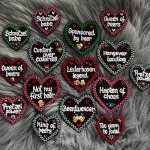 Könnte beinhalten: Eine Sammlung herzförmiger Lebkuchenherzen mit weißem Zuckerguss und Aufschriften wie "Schnitzel babe" und "Hangover loading". Die Lebkuchen haben dekorative Ränder und florale Verzierungen.