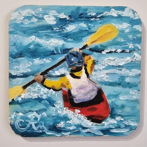 Op de afbeelding: Olieverfschilderij van een kajakker die door blauwe en witte golven peddelt. De kajakker draagt een geel en rood zwemvest en een blauwe helm. De peddel is geel. Het schilderij staat op een vierkant houten paneel.