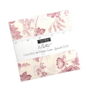 May include: A stack of fabric squares featuring a floral design in cream and mauve. The fabric is labelled "3 Sisters Favorites Vintage Linens Lavender Fields" with a ruler printed on the side.