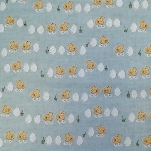May include: A blue and white fabric with a repeating pattern of yellow chicks and white eggs. The chicks are facing different directions and the eggs are scattered throughout the fabric.
