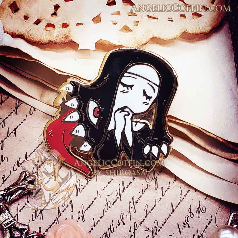 May include: Gold-tone enamel pin featuring a black-clad nun with a red and black monster emerging from her mouth. The pin has the text "AngelicCoffin.com by Shiroasa" on the bottom.