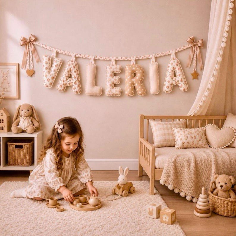 May include: A child's bedroom scene with a banner spelling "VALERIA" above a wooden bed. The room is decorated in soft beige tones, with a plush bunny, a wooden toy car, and a tea set. A young girl is playing with the tea set on a fluffy rug.