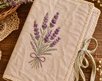 May include: A rectangular beige fabric cover featuring an embroidered bouquet of purple lavender sprigs tied with a bow. The edges are finished with a delicate cream-colored lace trim, and the cover includes a matching fabric ribbon tie closure.