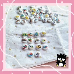 May include: A collection of white wooden buttons with colourful illustrations of vehicles and aeroplanes. The buttons are arranged in a circle on a white surface with a white and silver star pattern.