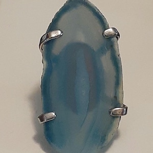 May include: A ring featuring a light blue agate stone set in a silver bezel. The stone has a natural, organic shape and is surrounded by a silver band.