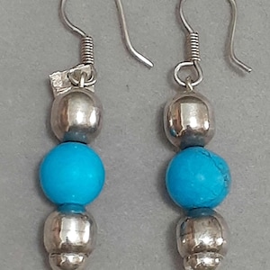 May include: A pair of silver dangle earrings with three beads each. The top and bottom beads are silver, and the middle bead is a bright turquoise blue.