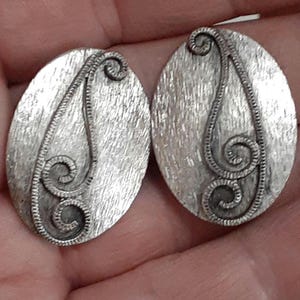 May include: A pair of silver oval-shaped earrings with a swirl design.