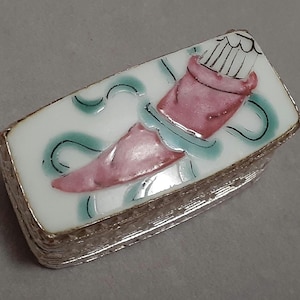 May include: A small rectangular box with a silver trim and a white porcelain top. The top features a painted design of a pink and green flower with a white center.