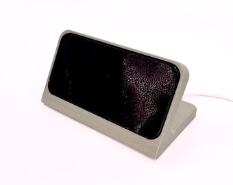 May include: A gray phone stand with a black screen. The stand is made of a textured material and has a raised edge around the screen.