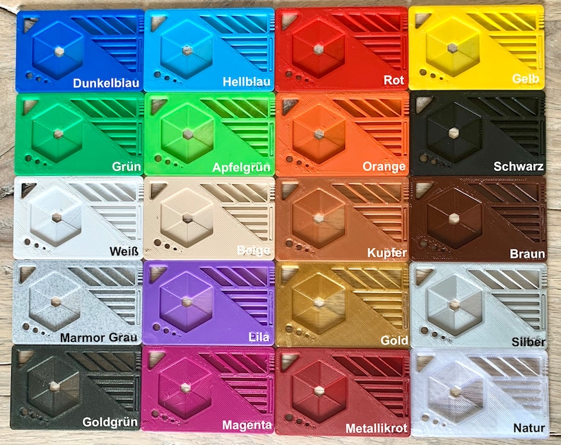 May include: A collection of 16 plastic cards, each with a different color and texture. The cards are arranged in a grid pattern and labeled with the color names in German. The colors include dark blue, light blue, red, yellow, green, apple green, orange, black, white, beige, copper, brown, marble gray, purple, gold, silver, gold green, magenta, metallic red, and natural.