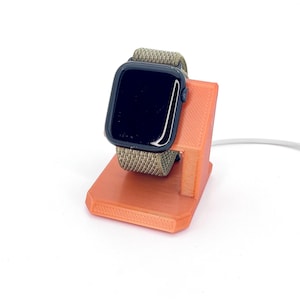 May include: An orange 3D printed charging stand for an Apple Watch with a black watch face and a green and black band.