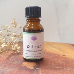 May include: An amber glass essential oil bottle with a black cap. The label displays the word "Retreat" and a lotus flower illustration. The bottle contains 100% pure essential oil blend. Website address: www.balancemehappy.com.au.