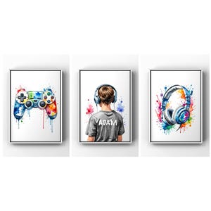 Op de afbeelding: Drie aquarellen op canvas met witte lijsten. De eerste afbeelding toont een kleurrijke videogamecontroller met aquarelverf die eraf druipt. De tweede afbeelding toont een persoon met een koptelefoon met de naam "ADAM" op de achterkant van zijn shirt. De derde afbeelding toont een kleurrijke koptelefoon met aquarelverf die eraf druipt.