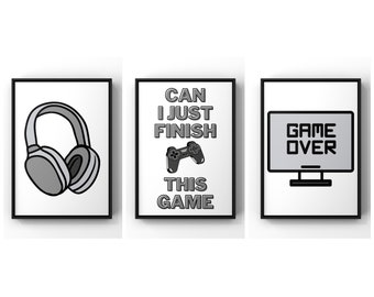Può includere: Tre stampe incorniciate nere con sfondi bianchi. La stampa a sinistra presenta un'illustrazione in bianco e nero di cuffie. La stampa al centro presenta un'illustrazione in bianco e nero di un controller per videogiochi con il testo "Can I Just Finish This Game". La stampa a destra presenta un'illustrazione in bianco e nero di un monitor per computer con il testo "Game Over".