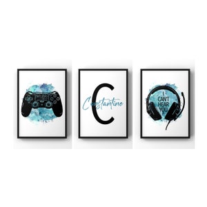 May include: Three framed prints with a blue watercolour background. The first print features a black video game controller. The second print features a black letter C with the word "Constantine" written in cursive. The third print features a black headset with the text "I can't hear you".