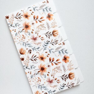May include: A white planner divider with a floral pattern featuring orange, brown, and gray flowers and leaves. The divider has five tabs for easy organization. The design is a watercolor style, perfect for stationery and office supplies.