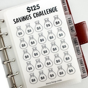 May include: A clear plastic savings challenge insert for a binder. The insert features the text "$125 SAVINGS CHALLENGE" and illustrations of money bags, each labeled with "$5". The insert is divided into sections with labeled tabs.