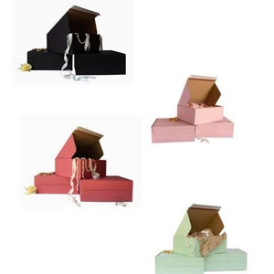 May include: Three sets of nested gift boxes in black, pink, and green. Each set has three boxes, with the top box open and a white string of pearls inside.