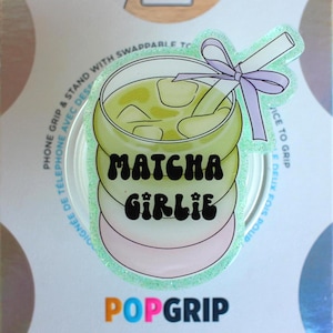 May include: A PopGrip phone accessory featuring a matcha drink design. The image shows a green drink with ice cubes, a straw, and a purple bow. The words "Matcha Girlie" are written in a retro font.