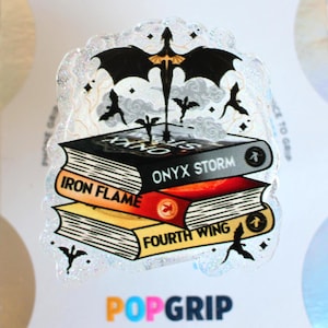 May include: A PopGrip featuring a stack of three books with the titles "Iron Flame", "Onyx Storm", and "Fourth Wing". The design includes a black bat-like figure with a gold accent and several smaller bat silhouettes. The PopGrip has a glittery, iridescent border.