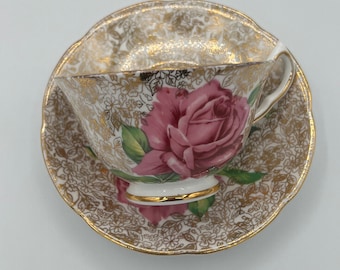 Puede incluir: Un juego de taza y platillo de té vintage con un diseño floral. La taza y el platillo son blancos con un borde dorado y un patrón de rosa rosa.