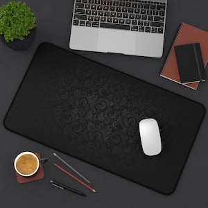 May include: A black desk mat with a decorative pattern, a white computer mouse, a cup of coffee, and pencils on a dark grey surface.