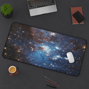 May include: A blue and gold galaxy-themed mousepad with a white computer mouse on top. The mousepad is on a dark gray surface.