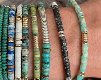 Op de afbeelding: Een set van negen kralenarmbanden in verschillende tinten groen, blauw en turquoise. De armbanden zijn gemaakt van verschillende materialen, waaronder metaal, steen en glas.