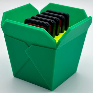 May include: A green takeout container with a lid open, revealing a stack of memory cards inside.