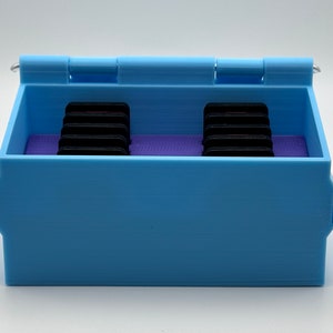 May include: A light blue plastic storage box with a hinged lid. The box has two rows of compartments inside, each containing a stack of black rectangular objects. The box is closed.