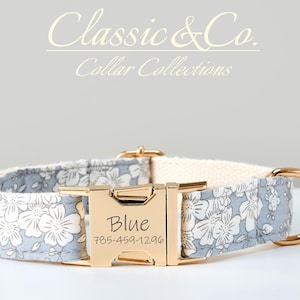 Könnte beinhalten: Ein Hundehalsband mit hellblauem Blumenmuster und einer goldfarbenen Schnalle. Das Halsband hat ein cremefarbenes Innenfutter und einen goldfarbenen Ring. Die Schnalle ist mit dem Namen "Blue" und einer Telefonnummer graviert. Der Text "Classic & Co. Collar Collections" steht oben.