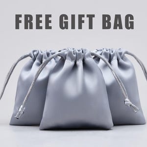 May include: Three silver satin drawstring gift bags. The bags are gathered at the top with a silver cord and have a small silver bead at the end of the cord. The text "FREE GIFT BAG" is above the bags.