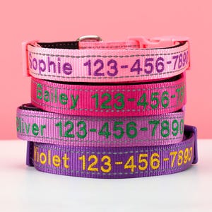 May include: Four stacked dog collars in pink and purple hues, each embroidered with a name and phone number. The collars are in varying shades, with contrasting text. The background is a soft pink.