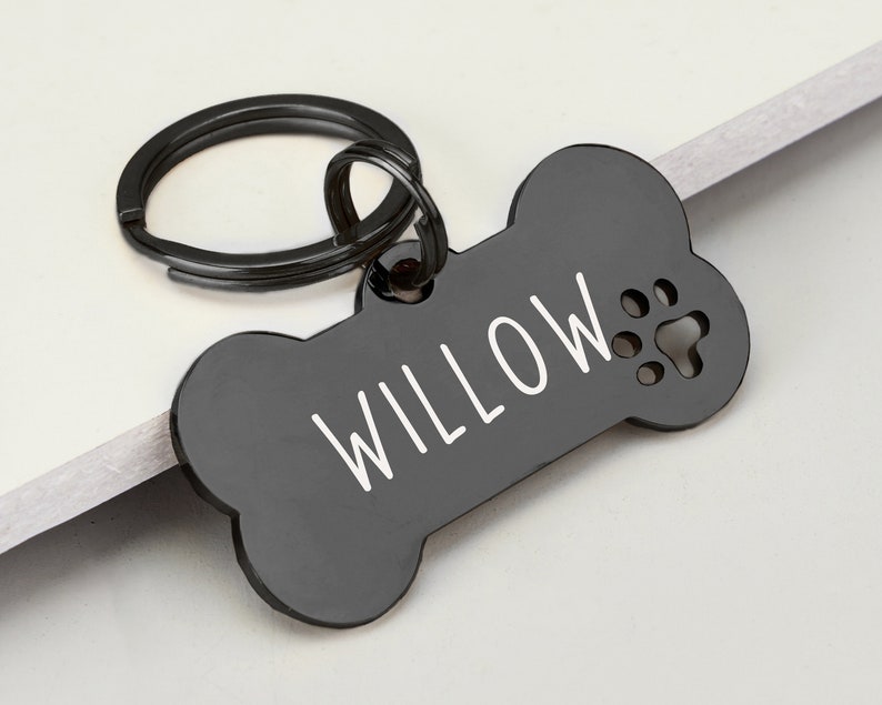 May include: Black bone-shaped dog tag with a silver key ring. The tag has the name "WILLOW" engraved in white lettering and a paw print cutout.