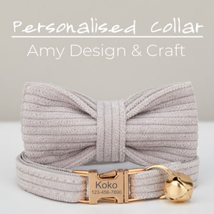 May include: A light gray cat collar with a matching bow tie. The collar has a gold buckle with the name "Koko" and a phone number engraved on it. The collar also has a gold bell.