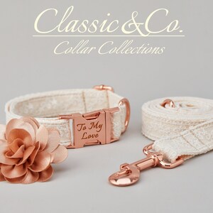 May include: A white dog collar and leash set with a rose gold buckle and a matching rose gold flower charm. The collar has the text "To My Love" engraved on the buckle. Classic & Co. Collar Collections.