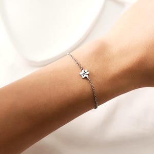 May include: A delicate silver bracelet featuring a paw print charm with the letter "A" in the center. The bracelet is worn on a wrist, showcasing its fine chain and minimalist design. The charm is small and detailed, adding a touch of charm.
