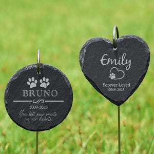 May include: Two black slate pet memorial garden stakes. One is round with the name "Bruno", paw prints, and the text "You left paw prints on our hearts". The other is heart-shaped with the name "Emily" and the text "Forever Loved".