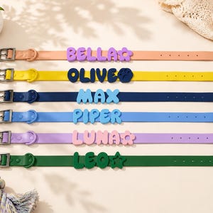May include: Six silicone pet collars in peach, yellow, navy, light blue, lavender, and dark green. Each collar features a metal buckle and custom raised lettering spelling BELLA, OLIVE, MAX, PIPER, LUNA, and LEO with flower, paw, and star icons.