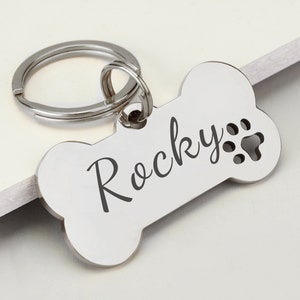May include: Silver bone-shaped dog tag with a split ring. The tag is engraved with the name "Rocky" and a paw print.