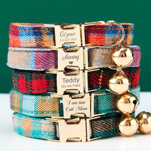 May include: A stack of colorful plaid dog collars with gold-colored buckles and attached bells. Each collar has a different plaid pattern in shades of red, blue, orange, and green. The buckles are engraved with pet names and contact information.