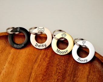 May include: Four personalized dog tag keychains with different designs and names: Willow, Daisy, Moose, and Honey. The keychains are made of metal and have a round shape.