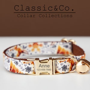 Puede incluir: Un collar de gato blanco y naranja con una hebilla y una campana doradas. El collar est&aacute; personalizado con el nombre "Anne" y un n&uacute;mero de tel&eacute;fono. Classic & Co. Collar Collections.