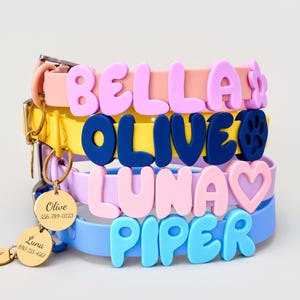 May include: A stack of four silicone pet collars in peach, yellow, lavender, and light blue. Each collar features large, raised, colorful letters spelling the names BELLA, OLIVE, LUNA, and PIPER, along with attached gold-toned circular metal ID tags.