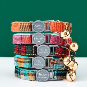 May include: A stack of colorful plaid cat collars with gold bells. Each collar has a gray buckle with a name and a phone number, or text like "Do not Feed". The collars are in shades of orange, pink, green, and teal.
