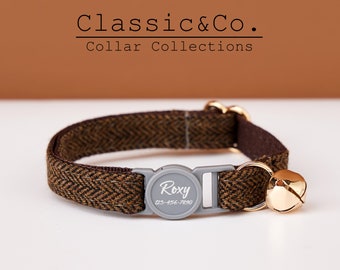 Puede incluir: Un collar de gato de color marrón y negro con estampado de espiga, con una hebilla gris y una campanilla dorada. La hebilla tiene el texto "Roxy" y un número de teléfono.